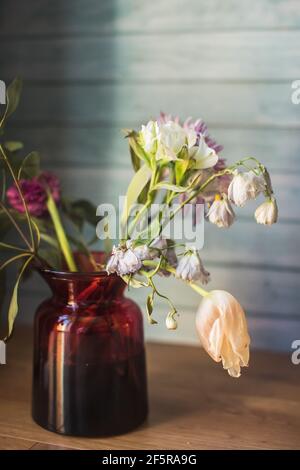 un bel bouquet sbiadito di fiori primaverili e delicato tulipani in vaso su sfondo di legno blu Foto Stock