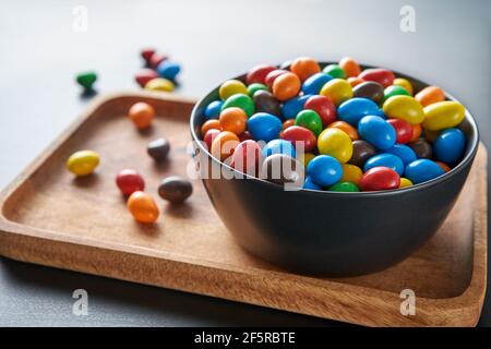 Una caramella luminosa cade in una ciotola nera su un vassoio di legno umore festoso. Foto Stock