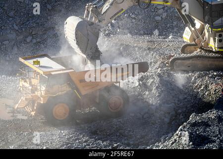 Le condizioni polverose come scavatrice carica dumper con minerale a. Miniera d'oro nell'Australia occidentale Foto Stock