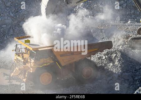 Le condizioni polverose come scavatrice carica dumper con minerale a. Miniera d'oro nell'Australia occidentale Foto Stock