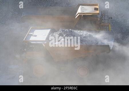 Le condizioni polverose come scavatrice carica dumper con minerale a. Miniera d'oro nell'Australia occidentale Foto Stock