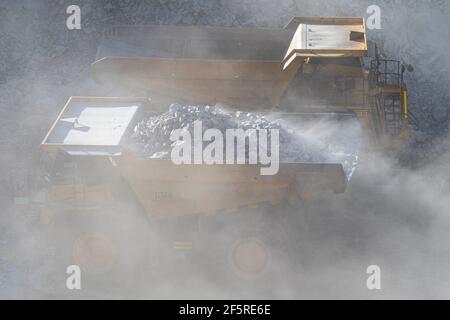 Le condizioni polverose come scavatrice carica dumper con minerale a. Miniera d'oro nell'Australia occidentale Foto Stock