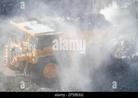 Le condizioni polverose come scavatrice carica dumper con minerale a. Miniera d'oro nell'Australia occidentale Foto Stock