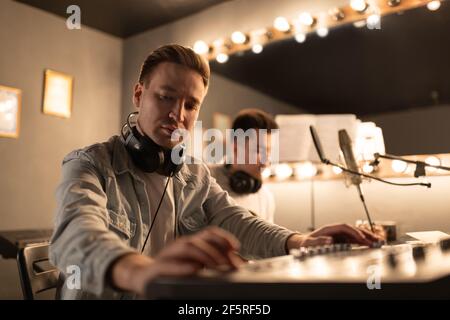 Musicista focalizzato che utilizza la scheda audio vicino a un collega Foto Stock