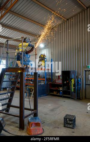 Boilermaker in abbigliamento protettivo utilizzando macinacaffè su scala metallica Foto Stock