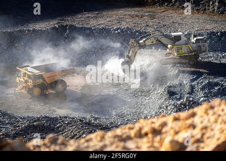 Le condizioni polverose come scavatrice carica dumper con minerale a. Miniera d'oro nell'Australia occidentale Foto Stock