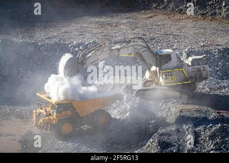 Le condizioni polverose come scavatrice carica dumper con minerale a. Miniera d'oro nell'Australia occidentale Foto Stock