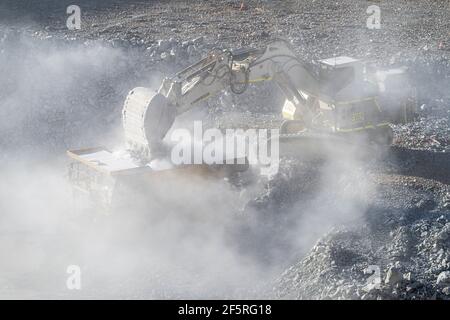 Le condizioni polverose come scavatrice carica dumper con minerale a. Miniera d'oro nell'Australia occidentale Foto Stock