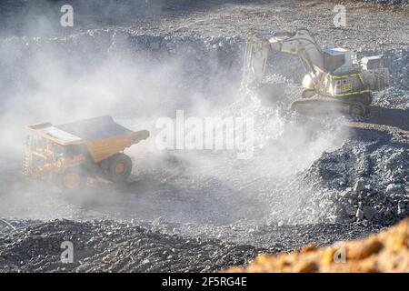 Le condizioni polverose come scavatrice carica dumper con minerale a. Miniera d'oro nell'Australia occidentale Foto Stock