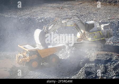 Le condizioni polverose come scavatrice carica dumper con minerale a. Miniera d'oro nell'Australia occidentale Foto Stock