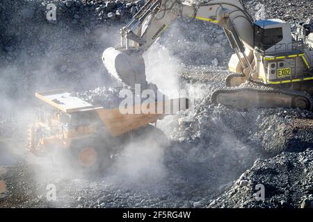 Le condizioni polverose come scavatrice carica dumper con minerale a. Miniera d'oro nell'Australia occidentale Foto Stock