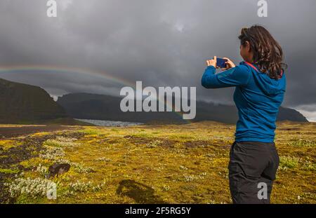 Donna scattando foto sul suo smartphone di arcobaleno in Icland Foto Stock