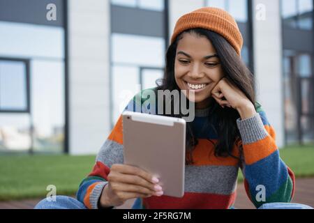 Bella donna afroamericana che usa un tablet digitale, guardando film all'aperto. Blogger influencer di successo video in streaming, comunicazione online Foto Stock