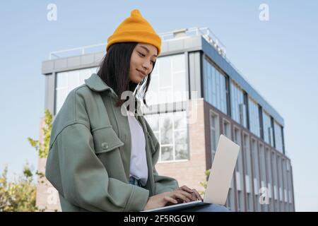 Donna asiatica che usa un computer portatile, cercando online. Giovane copywriter che scrive, lavorando progetto freelance all'aperto. Studente universitario che studia Foto Stock
