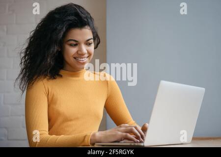 Bella donna afroamericana che usa il computer portatile, guardando corsi di formazione online. Ritratto di un giovane programmatore di successo che lavora da casa Foto Stock