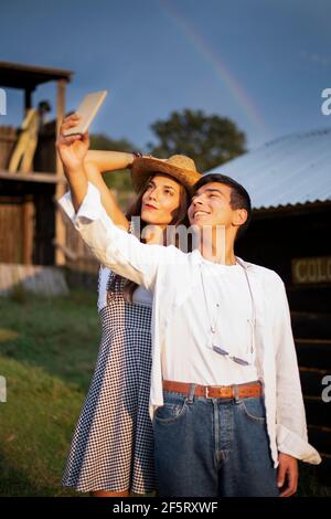 Due amici sorridono e scattano foto selfie nel ranch. Arcobaleno sul cielo Foto Stock
