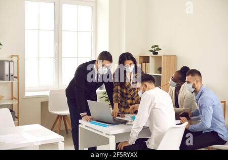 La squadra della gente di affari che indossa la maschera mentre lavora insieme dentro ufficio Foto Stock