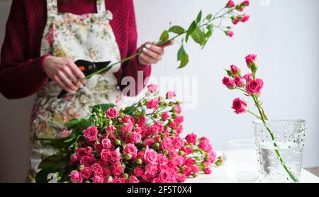 Primo piano della mano di una fiorista in un grembiule di fiori taglia i gambi di un bouquet di rose rosa con Cesoie in un negozio di fiori a work.Concept del wor Foto Stock