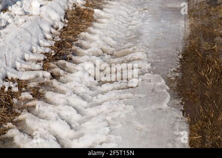 Le ruote del trattore si cingono su neve in fusione e terreno buio. Foto Stock