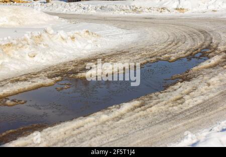 Un grande puddle su una strada innevata all'inizio della primavera Foto Stock