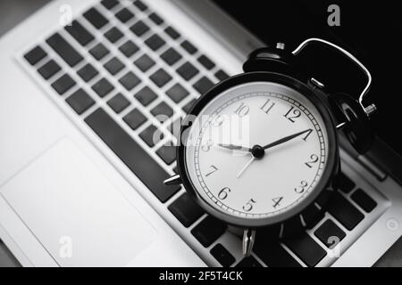 Orologio sulla tastiera del laptop per la tecnologia del computer con il concetto di orario di lavoro dell'ufficio aziendale. Foto Stock