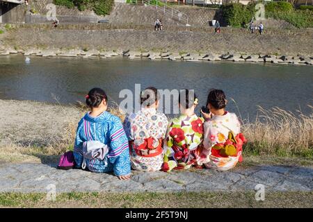 Quattro giovani donne che siedono sulle rive del Kamogawa (fiume Kamo) a Kyoto, Giappone. Foto Stock