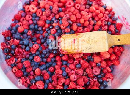 Lamponi e ribes nero in una ciotola con un pestello, facendo marmellata fatta in casa Foto Stock