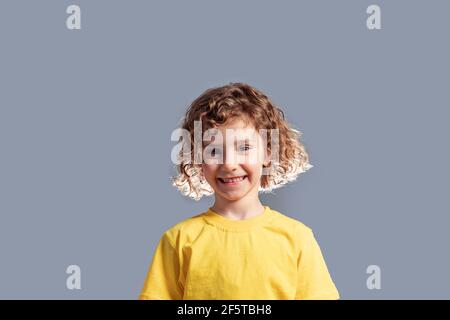 Adorabile bambino di 5 anni in T-shirt gialla in posa su grigio Foto Stock