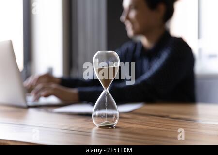 Primo piano su tempo di misurazione clessidra, donna d'affari indiana che lavora Foto Stock