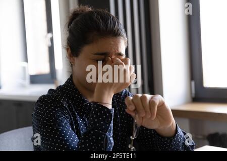 Primo piano esausta donna indiana massaggiante ponte nasale, tenendo bicchieri Foto Stock