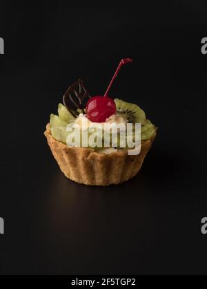 Torta da dessert alla frutta con ciliegie, foglia di shecolade, zeppe kiwi e crema proteica, su sfondo nero isolato Foto Stock