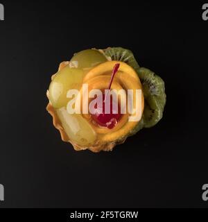 Torta da dessert alla frutta con uve ciliegie, kiwi e agrumi, su sfondo nero isolato Foto Stock