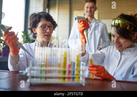Le giovani donne apprezzano il pipettaggio dei prodotti chimici in un'atmosfera rilassata presso il laboratorio universitario. Scienza, chimica, laboratorio, persone Foto Stock