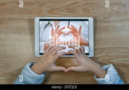 Il medico e il paziente scambiano gesti di riconoscimento e di amore durante la consultazione. Il cuore è piegato dalle palme. Videoconferenze online, utilizzando Internet sullo schermo di un tablet. Foto Stock