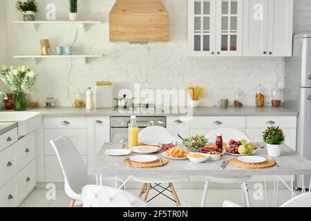 Colazione in stile latino sul tavolo. Interni moderni e luminosi con cucina bianca e dettagli in legno e bianco Foto Stock