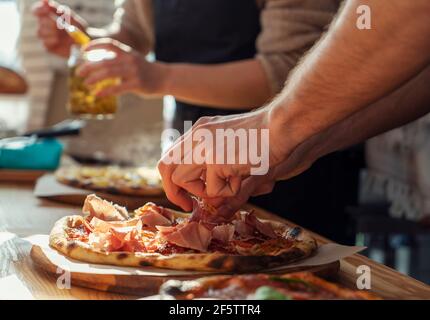 Primo piano di un uomo e di una donna stanno preparando la pizza in cucina in un ristorante, stendendo la carne e l'olio. In una giornata di sole Foto Stock