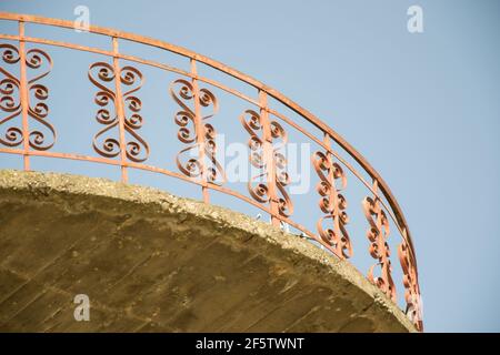 Moderno balcone rosso, recinzione in ferro battuto con forme cardiache contro il cielo blu, ringhiere, esterno di un edificio, pavimento incompiuto Foto Stock