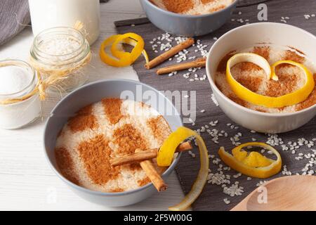 concetto di una vita morta di diverse ciotole di pudding di riso con riso sparso sul tavolo, fette di limone, un cucchiaio di legno e bastoncini di cannella Foto Stock