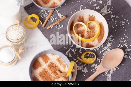 concetto di una vita morta di diverse ciotole di pudding di riso con riso sparso sul tavolo, fette di limone, un cucchiaio di legno e bastoncini di cannella Foto Stock