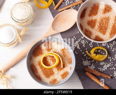 concetto di una vita morta di diverse ciotole di pudding di riso con riso sparso sul tavolo, fette di limone, un cucchiaio di legno e bastoncini di cannella Foto Stock