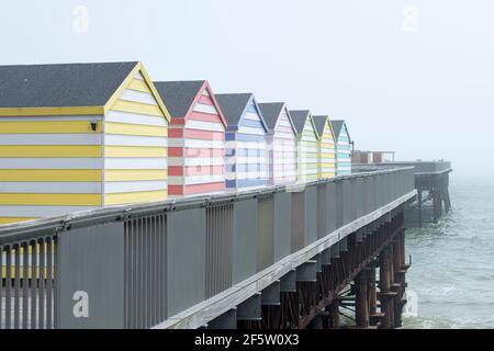 capanne di spiaggia di diversi colori su un molo nella nebbia con il mare sullo sfondo. Foto Stock
