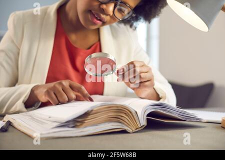 Giovane donna afro-americana Bbusiness leggere guardando attraverso la lente d'ingrandimento Foto Stock