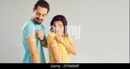 L'uomo e la donna mostrano le braccia dopo l'influenza o Covid-19 colpi in piedi su sfondo grigio dello spazio di copia Foto Stock