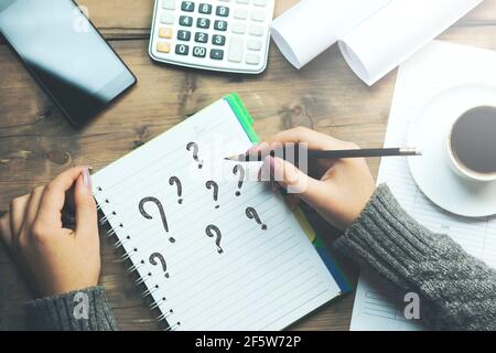 punto interrogativo sul notebook con la matita a mano donna e il telefono, il caffè e la calcolatrice sul tavolo Foto Stock