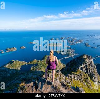 Lago Heiavatnet, case su piccole isole rocciose in mare, escursionista che guarda in basso dalla cima della montagna Festvagtind a Henningsvaer, Vagan Foto Stock