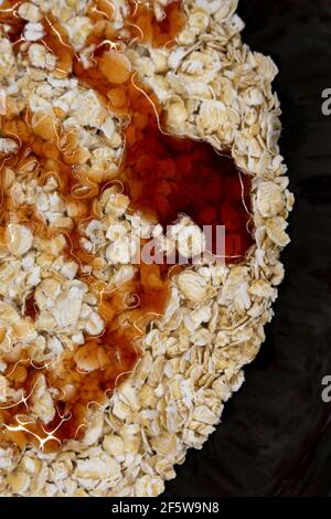 fiocchi d'avena in un piatto nero gocciolato con sciroppo o. miele Foto Stock
