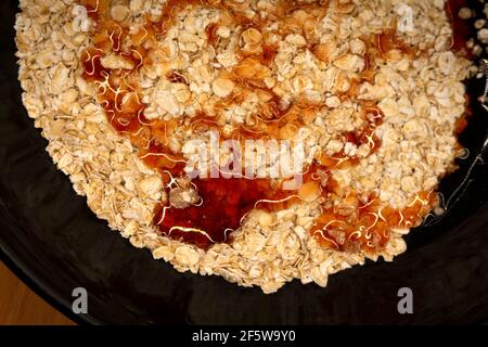 fiocchi d'avena in un piatto nero gocciolato con sciroppo o. miele Foto Stock