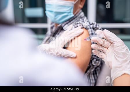 primo piano medico che tiene la siringa e l'uso di cotone prima di fare l'iniezione nella spalla del paziente anziano in maschera medica. covid-19 malattia del vaccino prepar Foto Stock