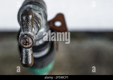 Messa a fuoco superficiale, vista macro della maniglia di un rubinetto d'acqua esterno, situato all'esterno di una casa colonica. L'usura pesante è visibile sulle aree della maniglia. Foto Stock