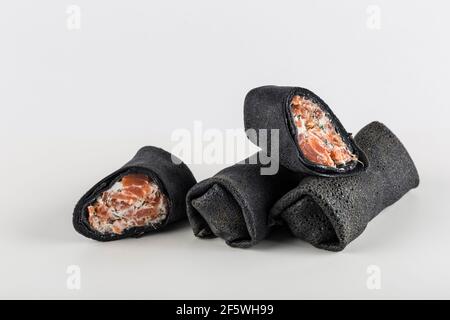 Frittelle nere di seppie con ripieno di salmone con formaggio cottage su sfondo bianco primo piano con spazio di copia per il testo, isolato. Tradizionale f Foto Stock